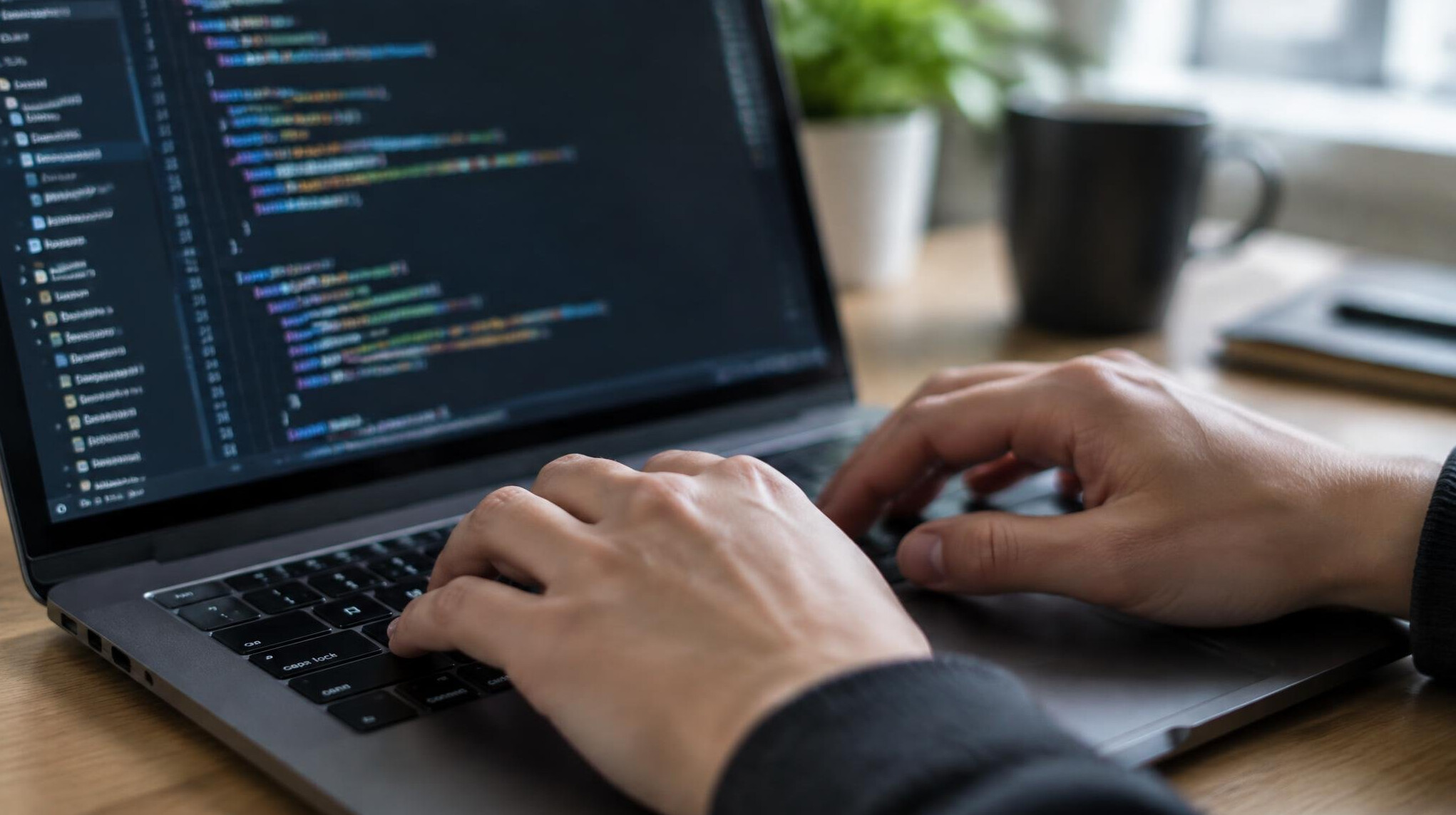 Close-up of hands typing on a laptop keyboard with code on the screen